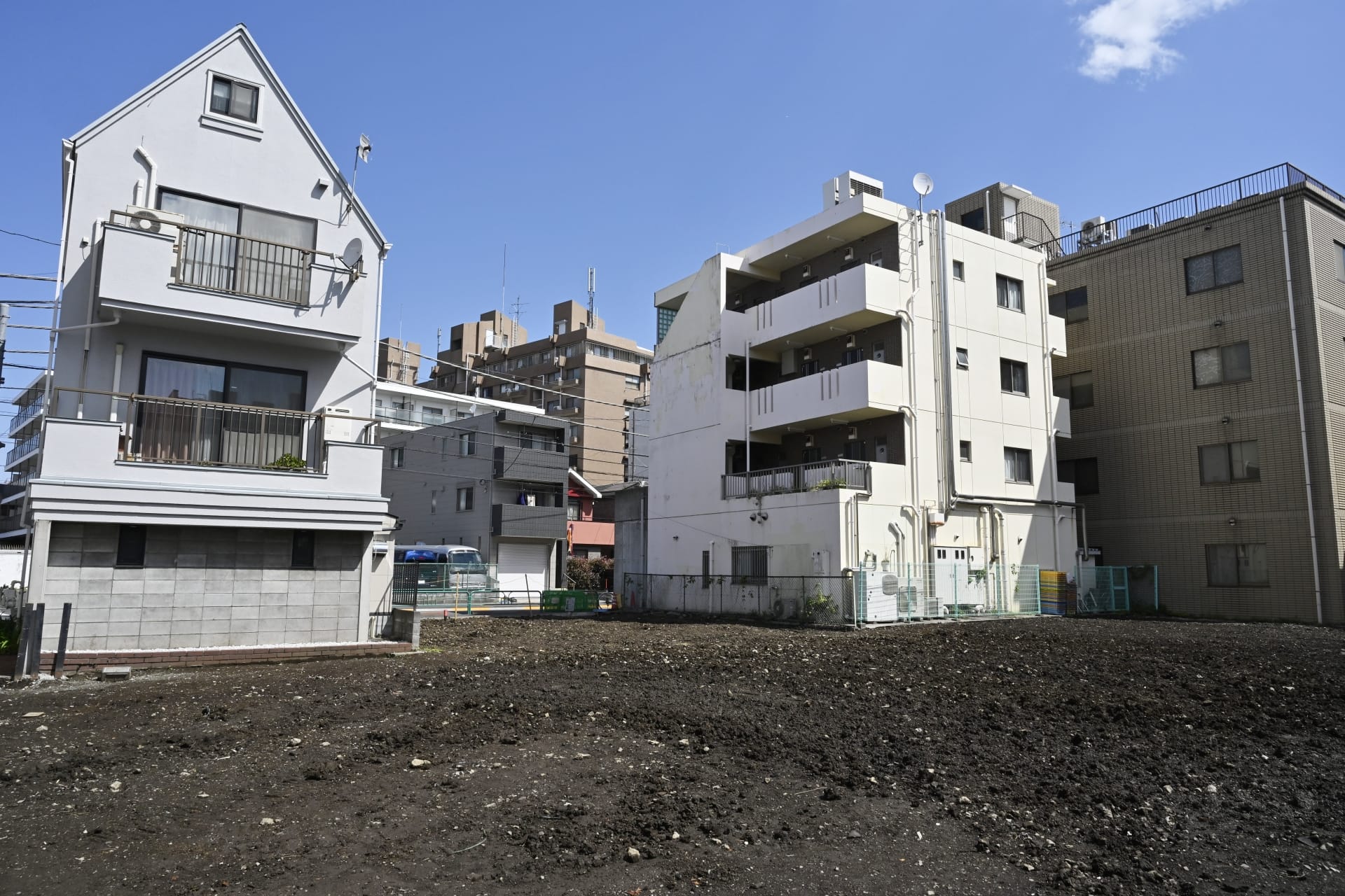 更地になった都市部の空き地の奥に、複数の中高層住宅が建ち並んでいる