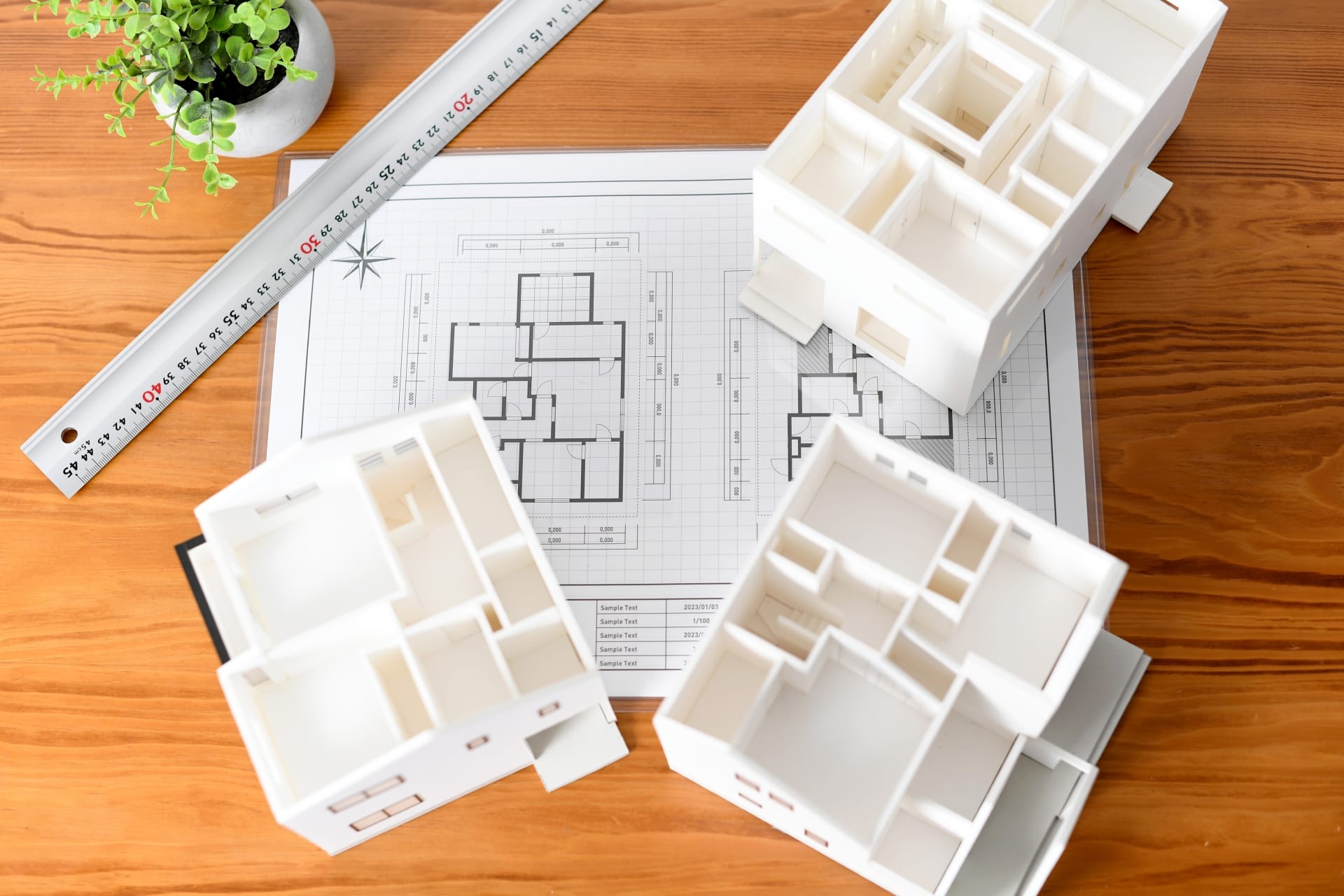木製の机の上に、住宅の間取り図と白い建築模型が3つ置かれている